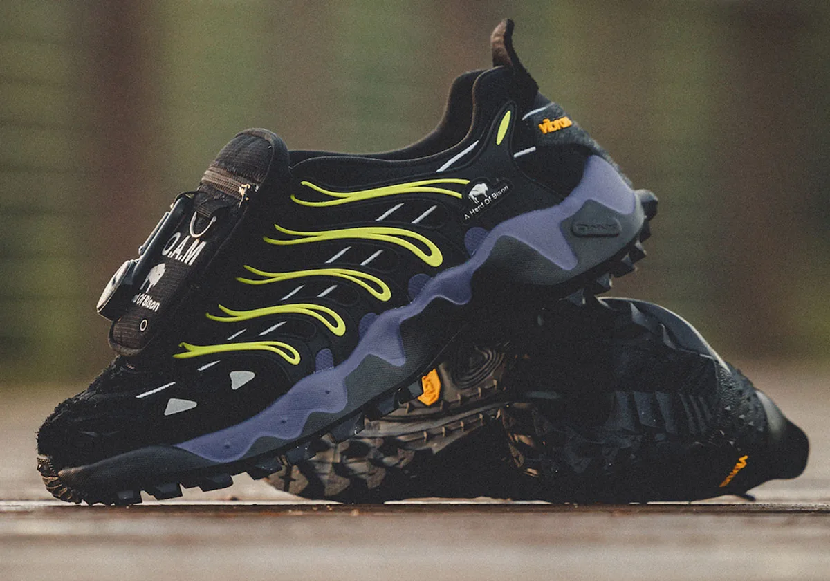 Lateral view of shoe resting on its mate on wood, neon yellow ribs, orange Vibram logo, Reebok DMX Trailzilla