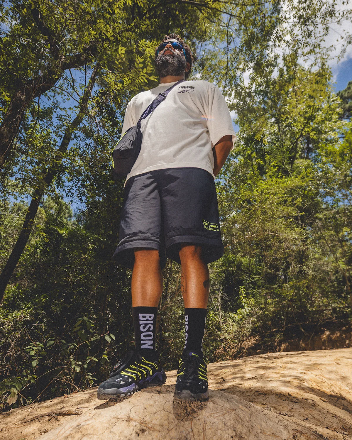 Low-angle on-foot shot of man in forest, BISON socks, black shorts, shoes on dirt mound, Reebok DMX Trailzilla