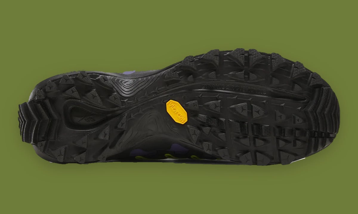 Outsole on green backdrop, black lugged tread with yellow Vibram hexagon logo, Reebok DMX Trailzilla