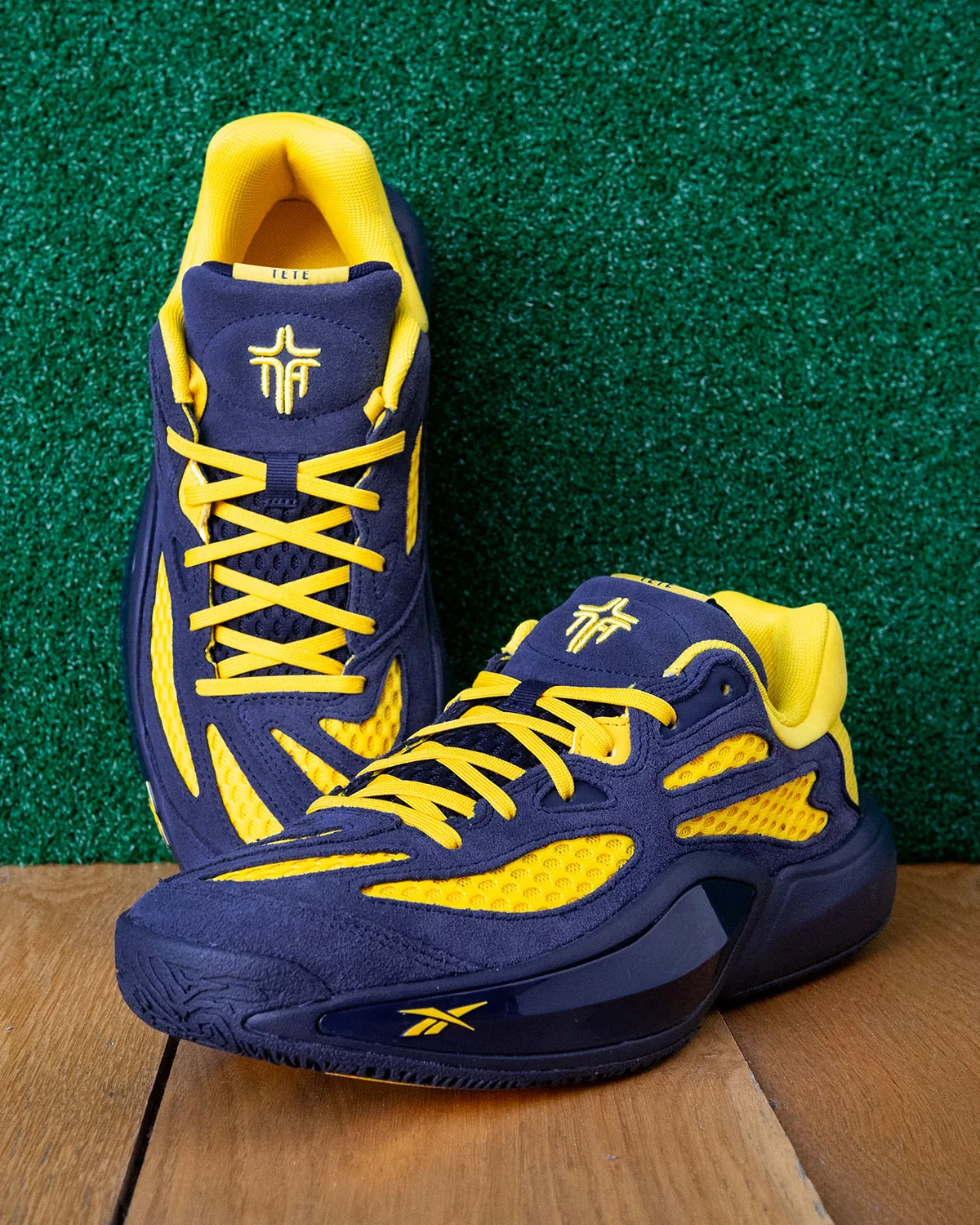 Pair on wood floor against green turf wall, navy suede, yellow mesh and Reebok logo, Brew Crew