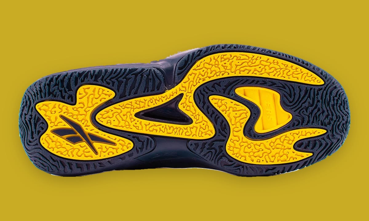 Outsole view, navy tread with yellow swirled pods, Reebok logo at heel, mustard backdrop, Brew Crew