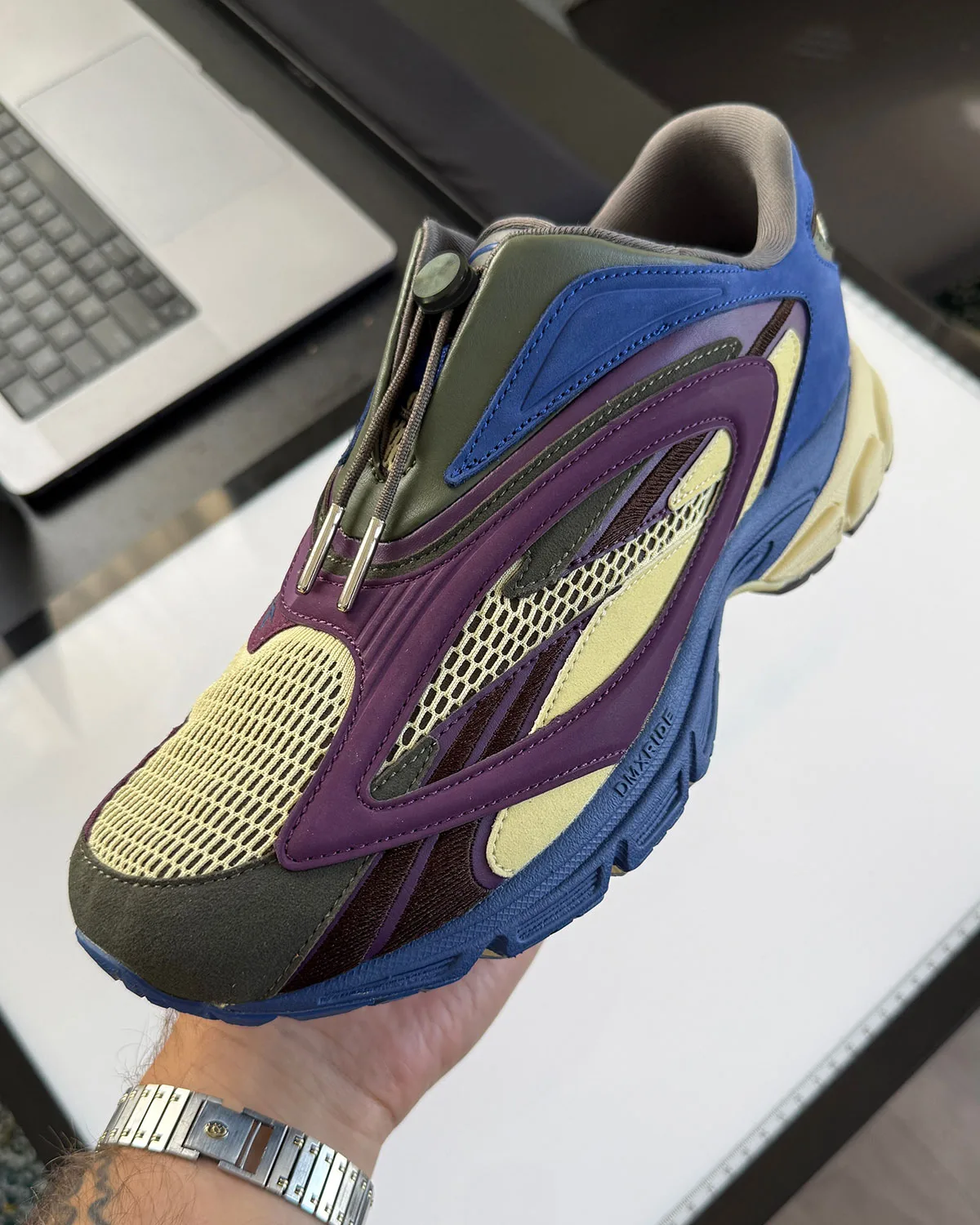Lateral view held in hand: purple overlays, cream mesh, blue midsole, toggle laces, DMX RIDE text, Purple Suede