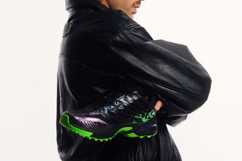 Model in a black leather jacket holding a black Salomon ACS NEXXT with bright green sole accents