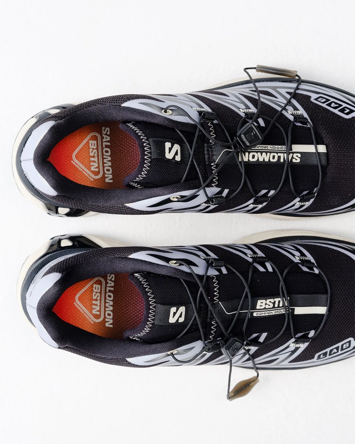 Top-down close crop of pair, orange gradient BSTN insoles, SALOMON and BSTN lace tags, 5 AM