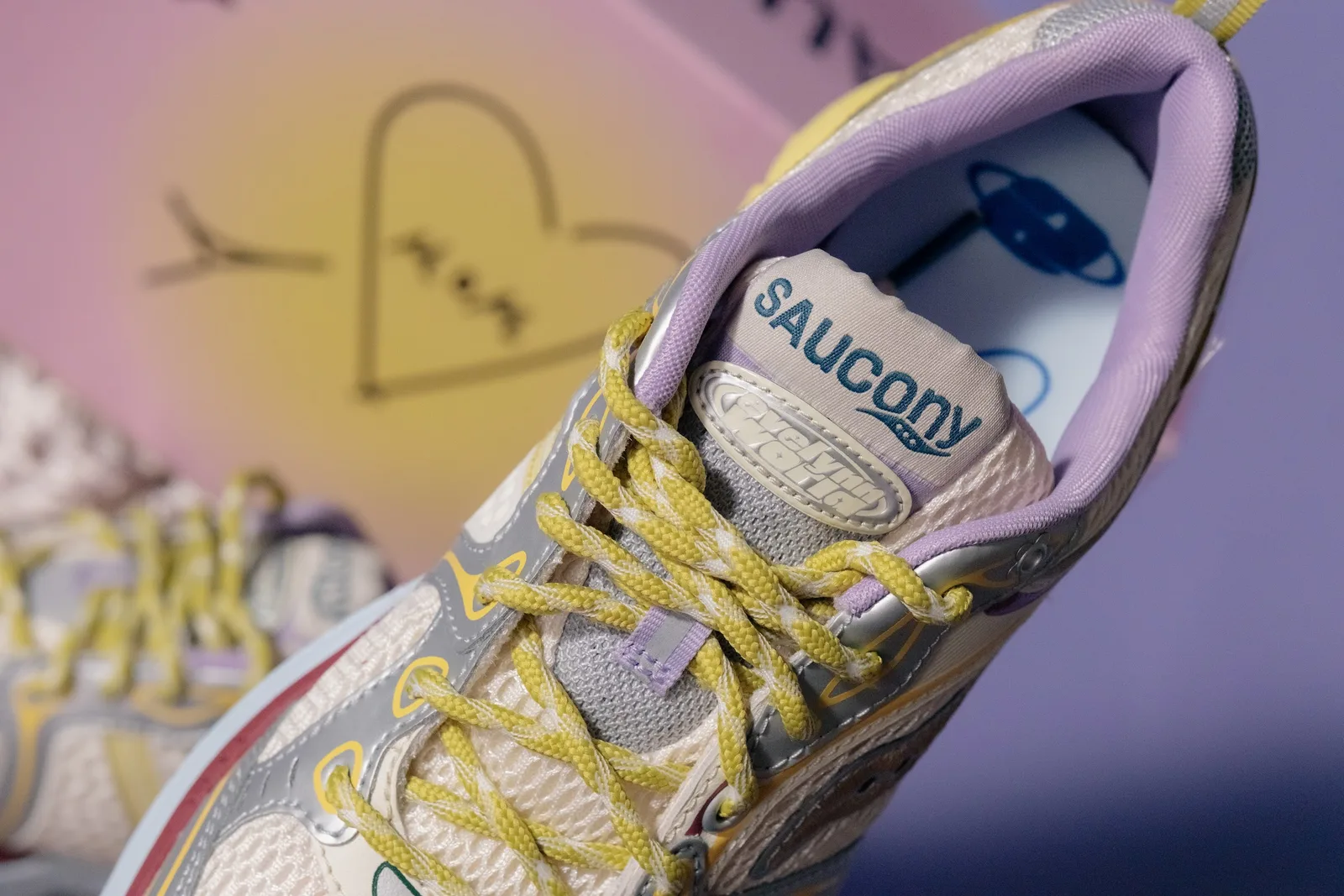Detail of tongue and laces: yellow braided laces, lilac lining, Saucony tongue label, pink and yellow box behind, x Evelynn