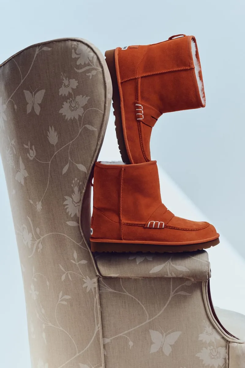 Orange suede loafer boots balanced on a floral wingback chair, one upright and one tilted, with white stitching on the
