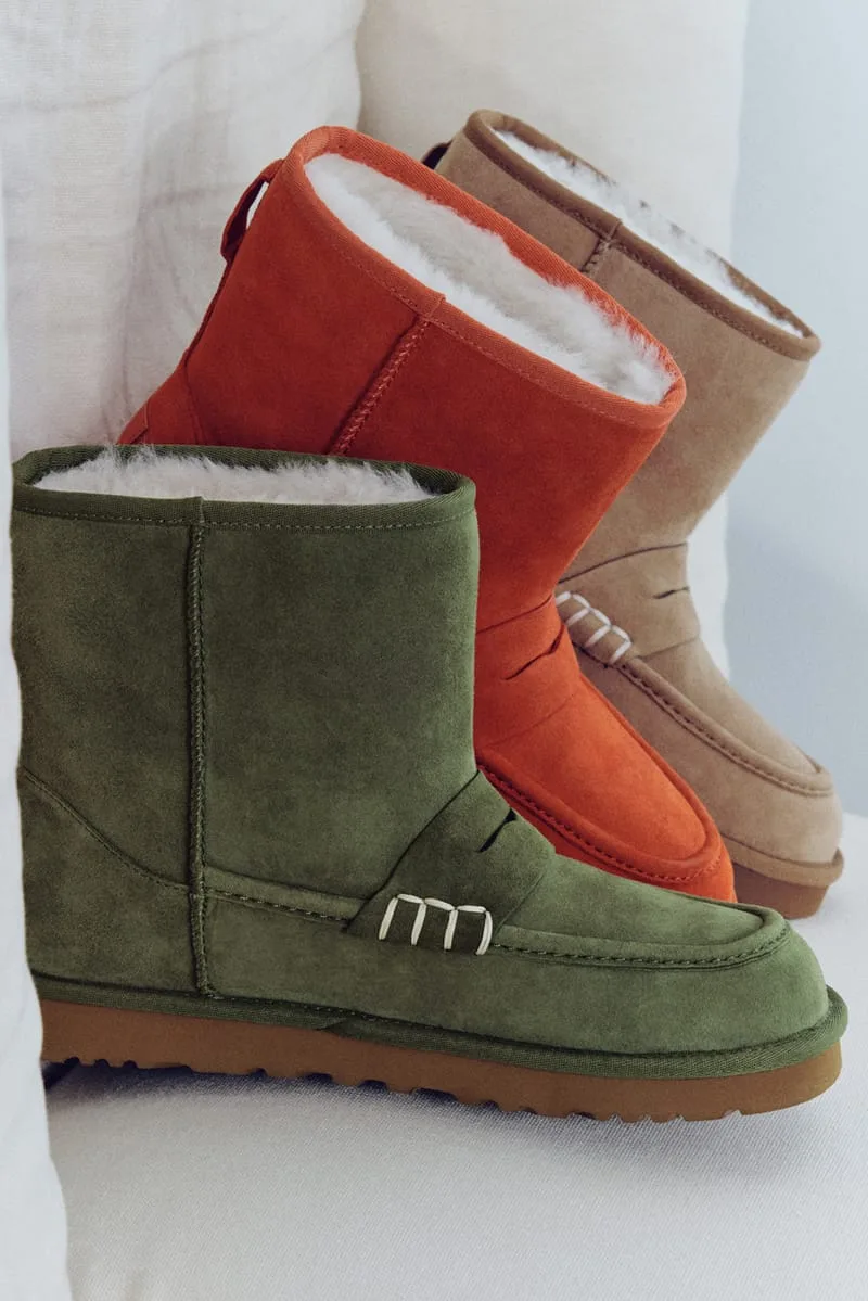 Three suede loafer-style boots in green, orange and tan on a cream chair, with white lacing and shearling visible at the, x