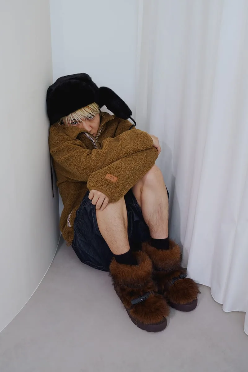On-foot shot of model seated in corner wearing brown fur boots with black buckles and a black fur hat, Heritage Utility Grizz