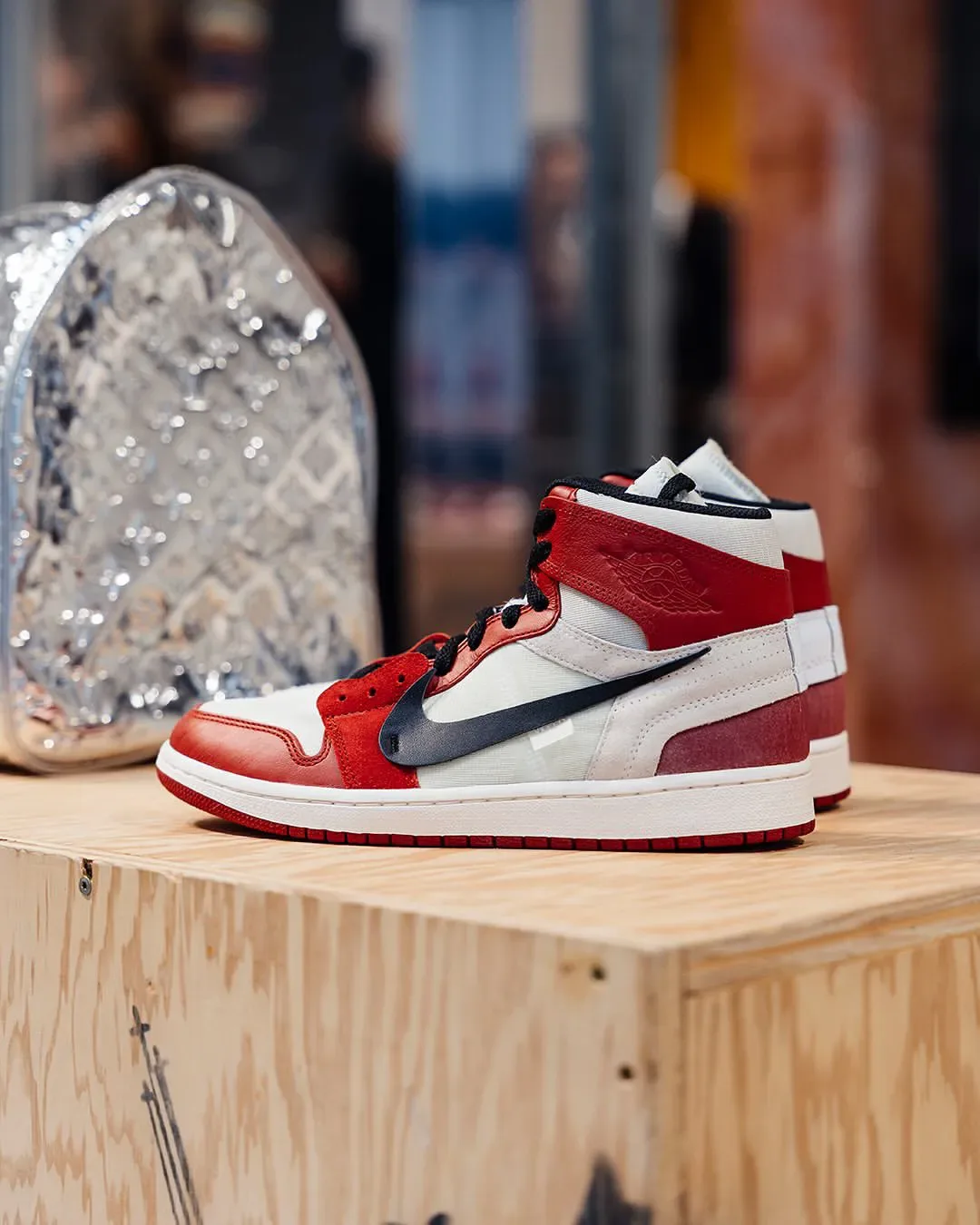 Medial view of red and white high-top on a wooden crate, black swoosh, sequined silver bag behind, Abloh: The Codes